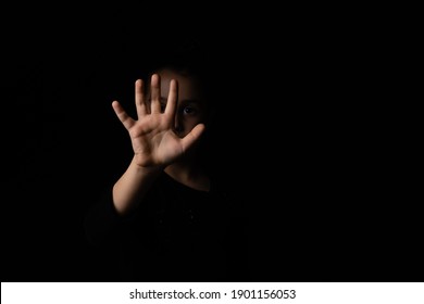 little girl with a raised hand making a stop sign gesture on a black background. Violence, harassment and child abuse prevention concept.