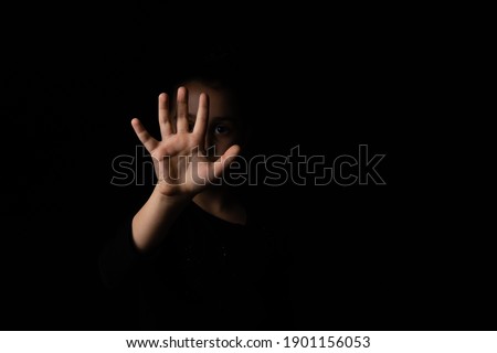 little girl with a raised hand making a stop sign gesture on a black background. Violence, harassment and child abuse prevention concept.