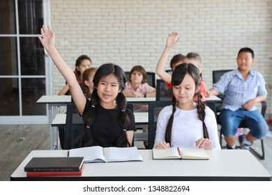 little girl raising hands in classroom (education concept) 