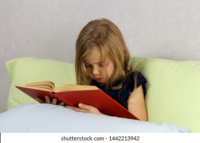 Little Girl Is Reading A Big Red Book In Bed.