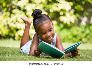 Little girl reading a book lying at park