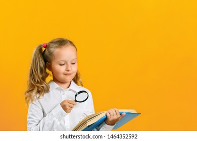 Little girl is reading a book on the table with a magnifying glass on a yellow background. The concept of education. Back to school. - Shutterstock ID 1464352592