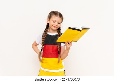 A little girl is reading a book on the German language. Courses on teaching German to children.A child in a jacket with a German flag.