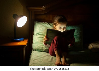 Little girl reads a book in bed. Child reads in the dark - Shutterstock ID 1901656213