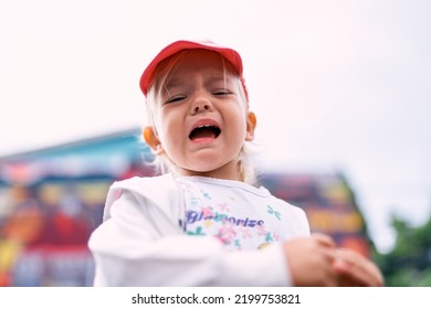 Little Girl In A Red Cap And White Tracksuit Whimpers