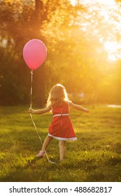 Little girl in a red dress holding a balloon. Happy and carefree childhood.