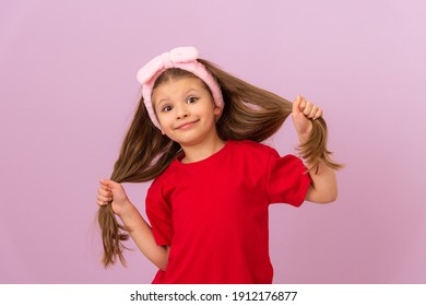 A little girl in a red T-shirt pulls her hair in different directions.