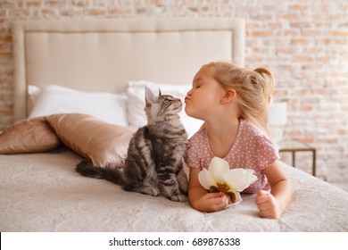 Little girl relaxing on the bed with her kitten. Child is kissing a cat