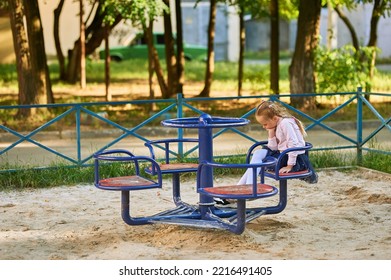 Little Girl Rides On A Swing Alone. A Girl In A Pink Blouse Sits On A Swing And Is Sad. She's Bored. High Quality Photo