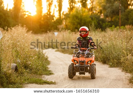 The little girl rides a quad bike ATV. A mini quad bike is a cool girl in a helmet and protective clothing. Electric quad bike electric car for children popularizes green technology.