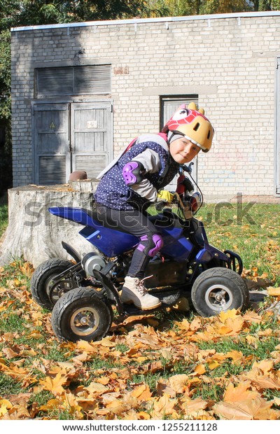 The little girl\
rides a quad bike. A mini quad bike is a cool girl in a helmet and\
protective clothing. Electric quad bike electric car for children\
popularizes green\
technology.