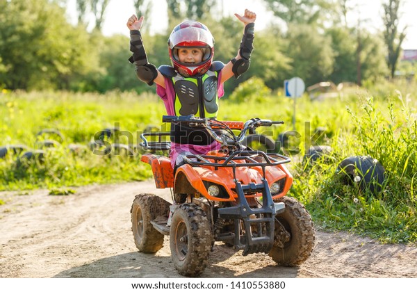 The little girl\
rides a quad bike. A mini quad bike is a cool girl in a helmet and\
protective clothing. Electric quad bike electric car for children\
popularizes green\
technology