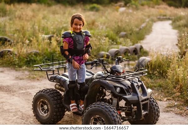 The little\
girl rides a quad bike ATV. A mini quad bike is a cool girl in a\
helmet and protective clothing. Electric quad bike electric car for\
children popularizes green\
technology.
