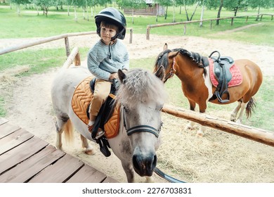 A little girl riding a miniature horse in nature. A charming little girl is sitting on a pony. A cute four-year-old girl is taking outdoor riding lessons at a ranch. Sports entertainment for children - Powered by Shutterstock