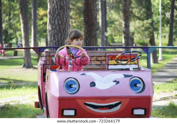Little girl is riding a\
pink toy car