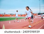 Little girl running over agility ladder during exercise class at the stadium.