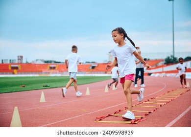 Little girl running over agility ladder during exercise class at the stadium. - Powered by Shutterstock