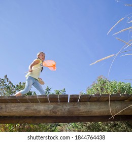 Little Girl Running Over A Wooden Bridge Holding A Fishing Net