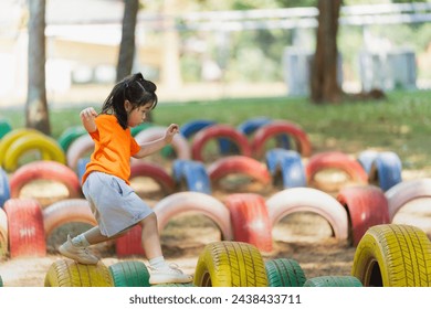 A little girl is running through a tire obstacle course. The tires are colorful and scattered around the area. The scene is playful and fun, with the girl enjoying herself as she navigates the course - Powered by Shutterstock