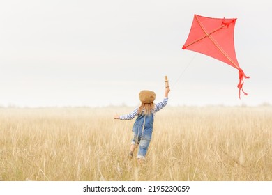 Little girl runs outdoors. Cheerful and happy child plays and launches a kite in the field against the blue sky. Kid dreams of flying and aviation.