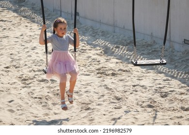 A Little Girl With A Sad Face Rides Alone On A Swing.