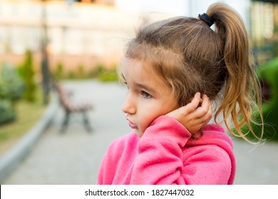 A Little Girl With A Sad And Frightened Face Holds Her Cheek With Her Hand - A Tooth Hurts. Ear Pain, Toothache, Swollen Cheek And Gums, Problems Of Pediatric Dentistry, Otolaryngology. Child Medicine