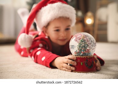 Little girl in Santa hat playing with snow globe on floor - Powered by Shutterstock