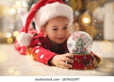 Little girl in Santa hat playing with snow globe on floor. Bokeh effect - Powered by Shutterstock