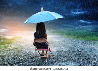 The Little Girl Sat In An Umbrella Chair Isolated In The Rain.