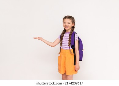 A Little Girl With A Satchel Behind Her Back Holds Your Advertisement On A White Isolated Background On Her Hand.