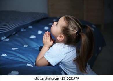 Little Girl Saying Bedtime Prayer Near Bed In Room At Night