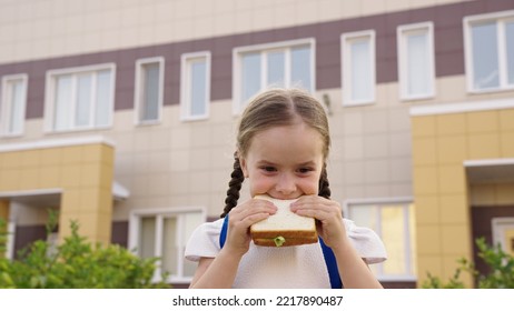 Little Girl With School Backpack Eats Sandwich At Recess School Yard. Children's Snack School Break. Kid Daughter Eats Delicious Breakfast. Healthy Pitakia Child Concept. Enjoyment Delicious Food