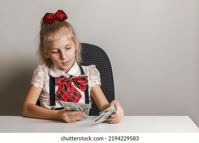 A Little Girl In A School Uniform Is Counting Money - Hundred-dollar Bills. Teaching Children Financial Literacy.