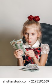 A Little Girl In A School Uniform Looks At The Money With Surprise And Admiration. Teaching Children Financial Literacy.