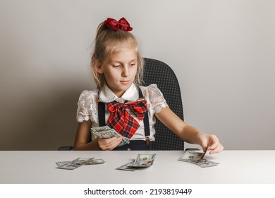 A Little Girl In A School Uniform Puts Money In Different Piles. Teaching Children Financial Literacy.