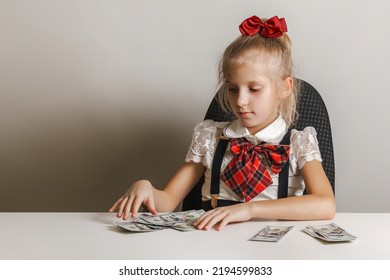 A Little Girl In A School Uniform Puts Money In Different Piles. Teaching Children Financial Literacy.