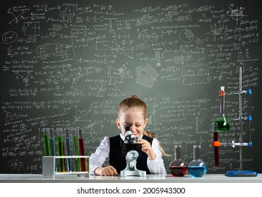 Little girl scientist looking through microscope in classroom at chemistry lesson. School chemical laboratory with glass flasks and test tubes. Schoolgirl making experiment in chemistry class. - Powered by Shutterstock