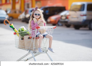 Little girl shopping with cart and bags. Child sitting in shopping cart near mall. Happy smiling child sitting in trolley cart. Sales and shopping