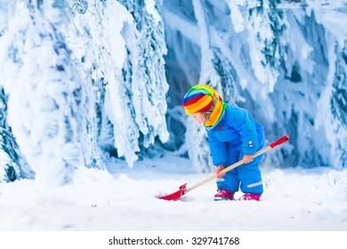 Little Girl Shoveling Snow On Home Drive Way. Beautiful Snowy Garden Or Front Yard. Child With Shovel Playing Outdoors In Winter Season. Family Removing Snow After Blizzard. Kids Play Outside.