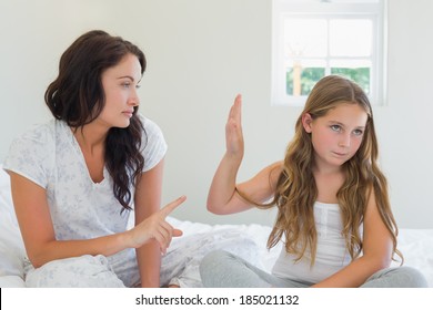 Little girl showing stop gesture to angry mother while sitting in bed at home