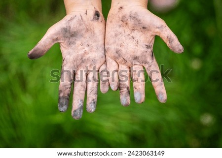A little girl shows her filthy hands stained with black ash from playing outdoors which will be difficult to wash off