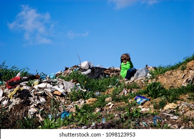 A Little Girl Sits Among A Garbage Dump