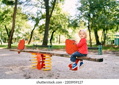 Little Girl Sits Turned Back On A Wooden Balance Beam In The Playground