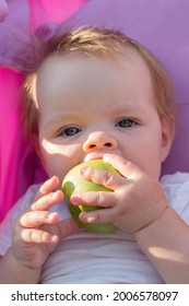 A Little Girl Sitting In A Baby Carriage With A Big Appetite Eats An Apple.