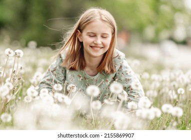 Little girl sitting in blowballs flowers field and smiling. Cute child kid with dandelions at nature