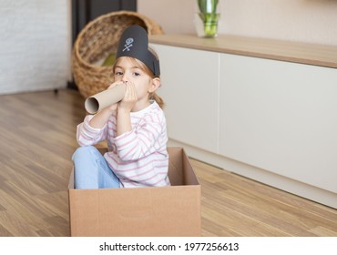 A Little Girl Sitting In A Cardboard Box Pretending To Be A Pirate Holding A Telescope.