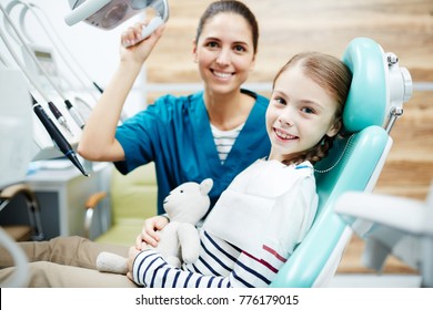 Little Girl Sitting In Chair At Dentist Office With Happy Doctor Near By