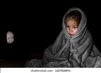 a little girl sitting in the dark wrapped in a blanket, in the background the blurred face of a scary doll. children's night fears