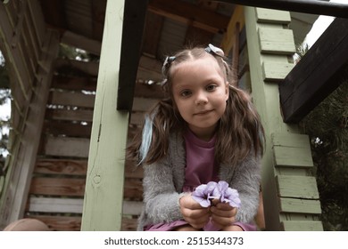 Little girl sitting in green wooden tree house and holding flowers in hands - Powered by Shutterstock