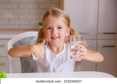 a little girl is sitting at home in the kitchen, pointing her finger up, holding a glass of water. Concept recommendation to drink water Child recommend drinking water. Good healthy habit for children - Shutterstock ID 1532345057